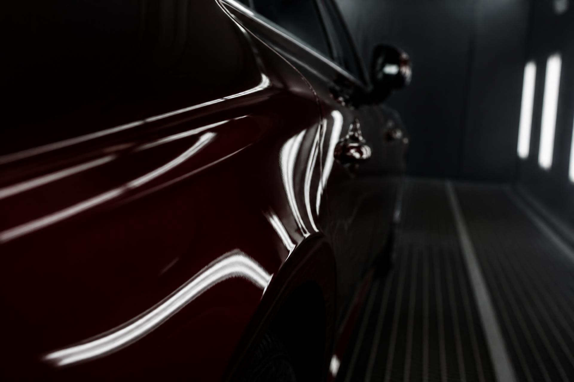 Deep gloss automotive paint reflecting booth lighting along a car's body line in a Chicago paint booth